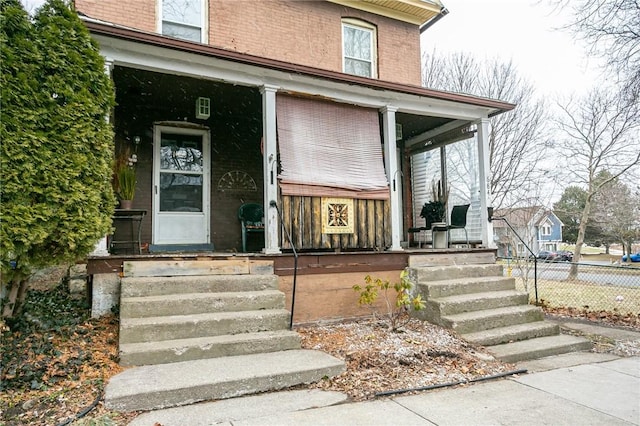 doorway to property with covered porch, fence, and brick siding