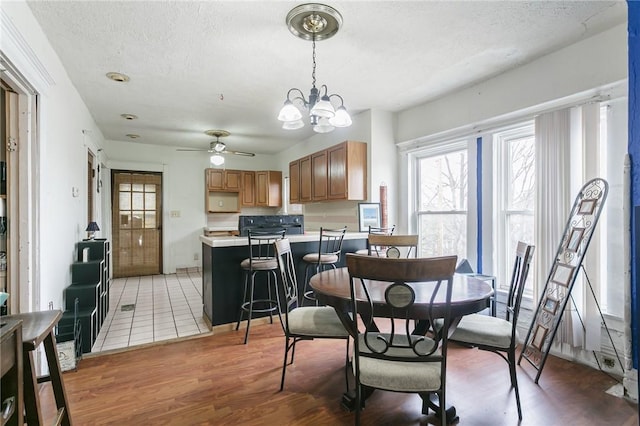 dining area with a textured ceiling, ceiling fan with notable chandelier, and light wood-style floors