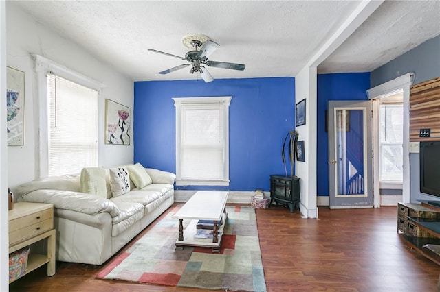 living room with a wood stove, ceiling fan, a textured ceiling, and wood finished floors