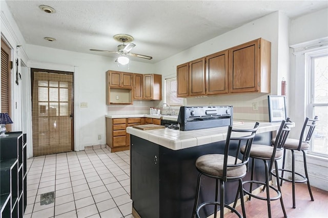 kitchen with a peninsula, a wealth of natural light, brown cabinetry, and tile counters