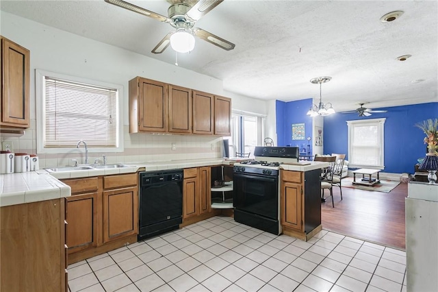 kitchen featuring tile countertops, a peninsula, a sink, dishwasher, and gas range oven