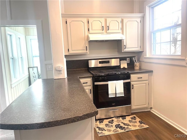 kitchen with dark wood-style flooring, dark countertops, a peninsula, under cabinet range hood, and stainless steel gas range oven