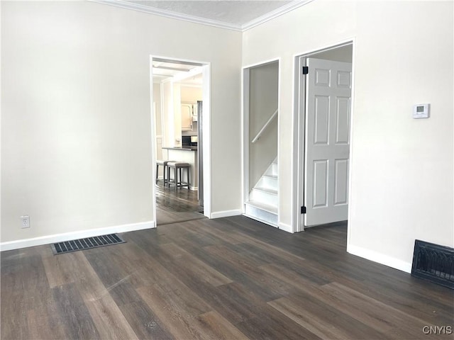 spare room featuring dark wood-style floors, crown molding, visible vents, baseboards, and stairs