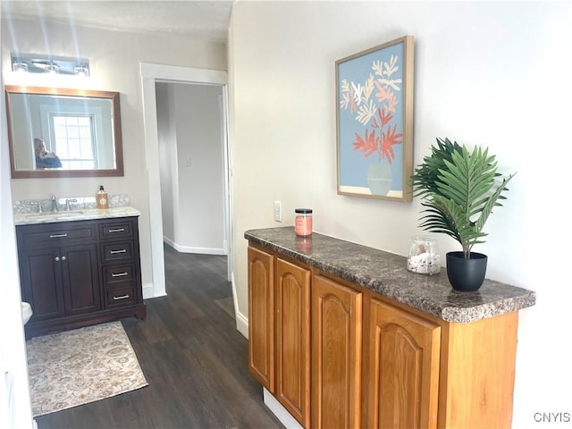 bar with dark wood-style floors, a sink, and baseboards