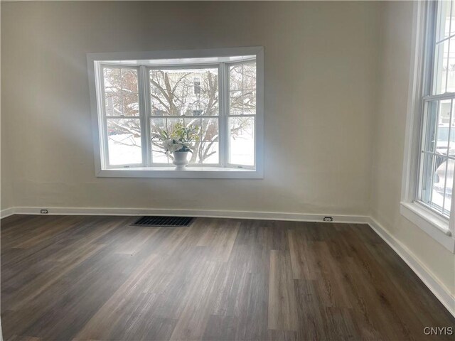 empty room with dark wood-style flooring, visible vents, and baseboards