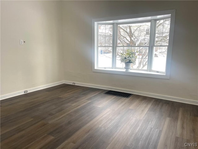 spare room featuring dark wood-style flooring, visible vents, and baseboards