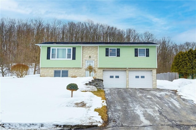 raised ranch featuring aphalt driveway, stone siding, fence, and an attached garage