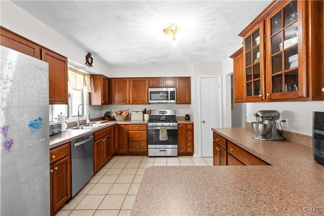 kitchen featuring brown cabinets, light tile patterned floors, stainless steel appliances, glass insert cabinets, and a sink