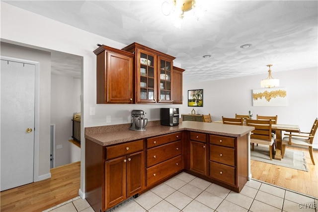 kitchen with light tile patterned floors, a peninsula, glass insert cabinets, and brown cabinets