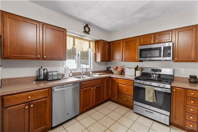 kitchen featuring appliances with stainless steel finishes, brown cabinetry, a sink, and light tile patterned floors