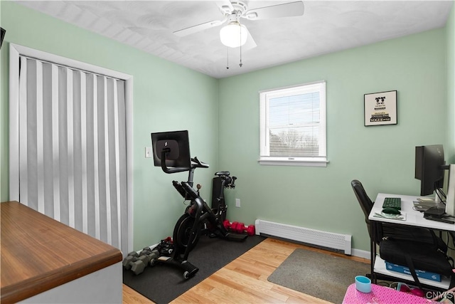 workout room with a baseboard heating unit, ceiling fan, and wood finished floors