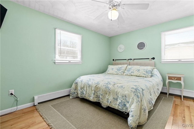 bedroom with baseboard heating, a baseboard radiator, wood finished floors, and baseboards