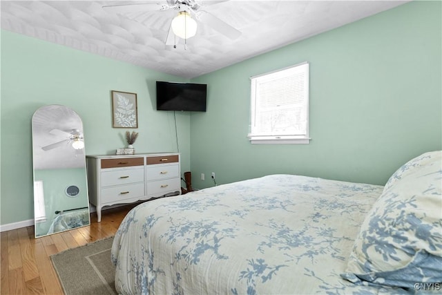 bedroom with hardwood / wood-style floors, a ceiling fan, and baseboards