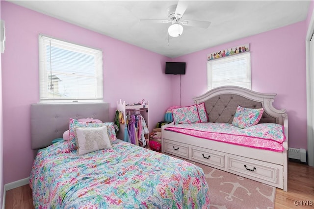 bedroom featuring light wood finished floors, multiple windows, a baseboard radiator, and a ceiling fan