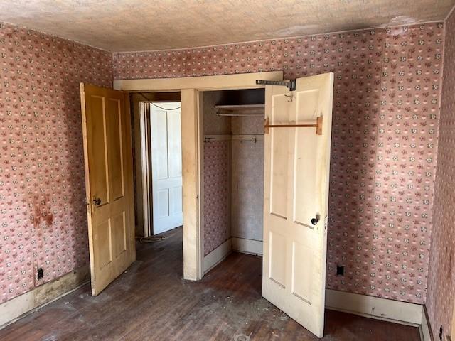 unfurnished bedroom with wallpapered walls, a textured ceiling, baseboards, and wood finished floors