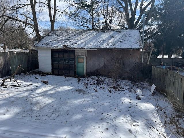 snow covered garage featuring a detached garage and fence