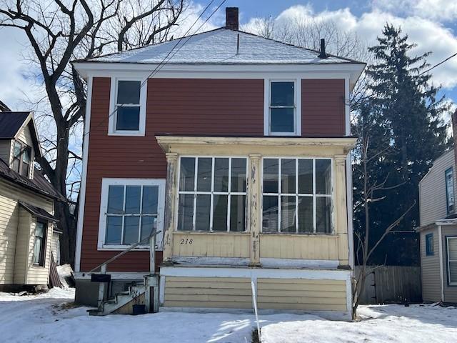 snow covered back of property with entry steps, a chimney, and a sunroom