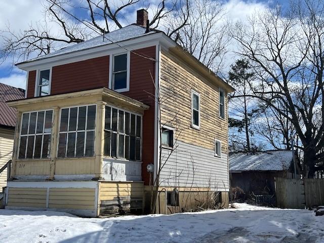 view of snow covered exterior with a sunroom and a chimney