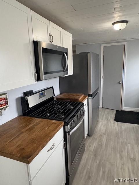 kitchen featuring butcher block counters, light wood-style flooring, appliances with stainless steel finishes, white cabinetry, and wooden ceiling