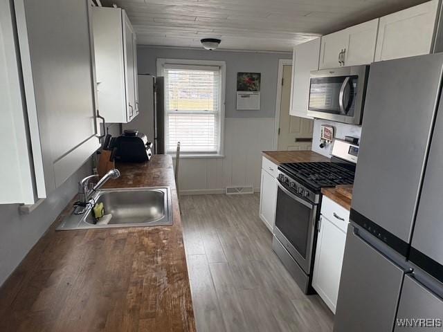 kitchen with visible vents, appliances with stainless steel finishes, white cabinets, a sink, and wood counters