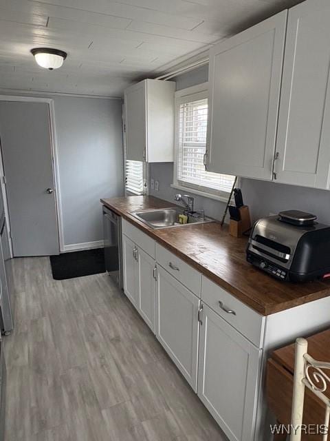 kitchen featuring light wood-style flooring, white cabinets, a sink, wood counters, and dishwashing machine