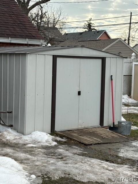 snow covered structure featuring a storage shed and an outbuilding