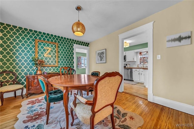 dining space featuring baseboards, wallpapered walls, an accent wall, and light wood-style floors