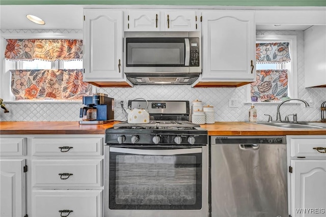 kitchen with wooden counters, appliances with stainless steel finishes, a sink, and white cabinets