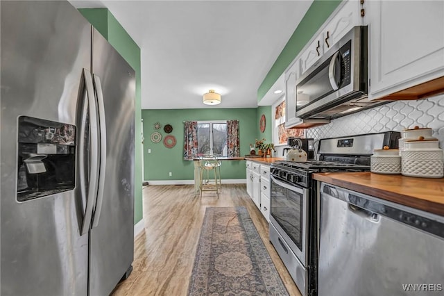 kitchen featuring tasteful backsplash, wooden counters, appliances with stainless steel finishes, white cabinetry, and baseboards