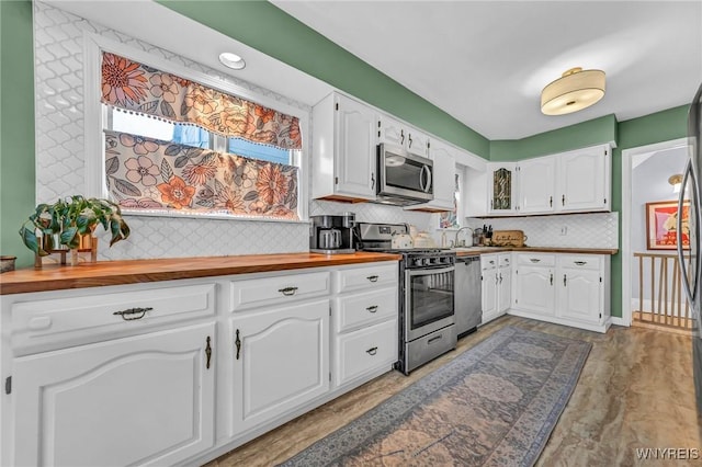 kitchen featuring stainless steel appliances, butcher block counters, white cabinets, and backsplash