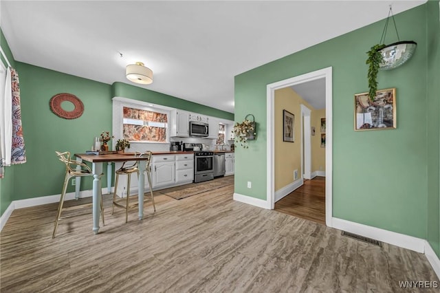 kitchen with visible vents, white cabinets, baseboards, light wood-style flooring, and stainless steel appliances