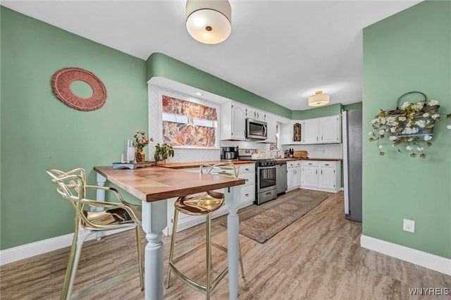 kitchen with appliances with stainless steel finishes, light wood-type flooring, white cabinets, and baseboards