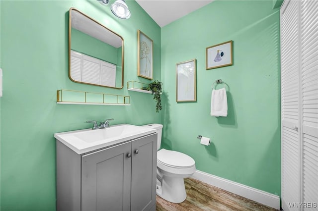 bathroom featuring toilet, wood finished floors, vanity, baseboards, and a closet