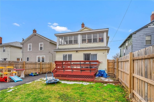 back of house with a trampoline, a chimney, a lawn, a deck, and a fenced backyard