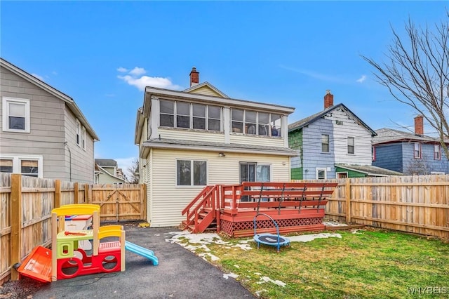 back of house featuring a deck, a chimney, a fenced backyard, and a lawn