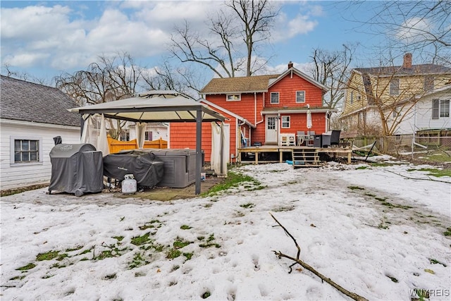 snow covered house with a gazebo, fence, a wooden deck, and a hot tub