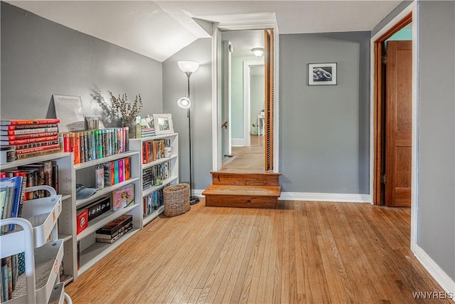 corridor featuring stairs, vaulted ceiling, baseboards, and wood finished floors