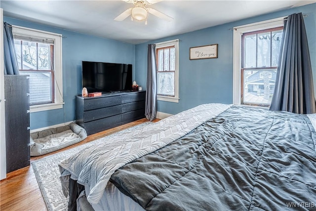 bedroom featuring multiple windows, wood finished floors, a ceiling fan, and baseboards