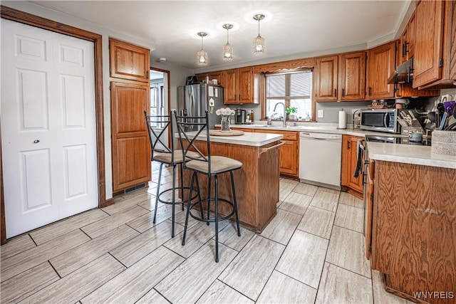 kitchen with appliances with stainless steel finishes, a breakfast bar, brown cabinets, light countertops, and a sink