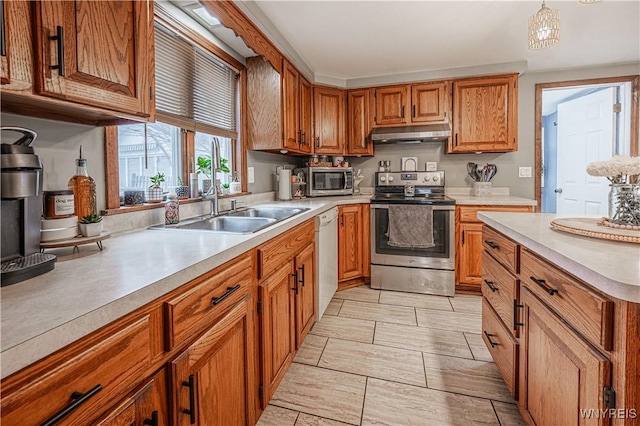 kitchen featuring brown cabinetry, appliances with stainless steel finishes, light countertops, under cabinet range hood, and a sink