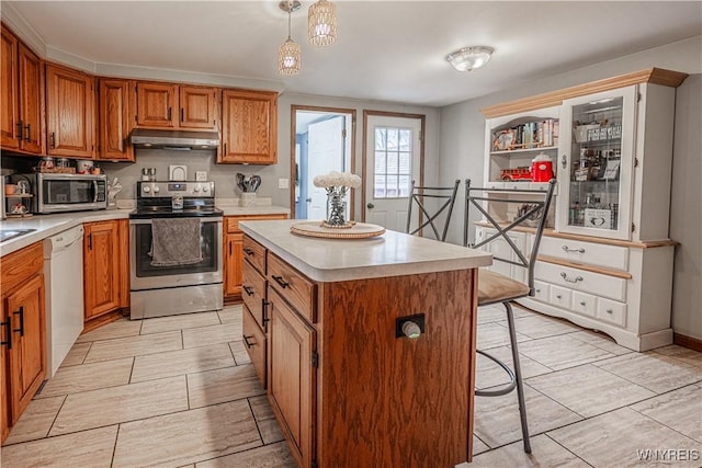 kitchen with brown cabinets, a breakfast bar area, stainless steel appliances, light countertops, and under cabinet range hood