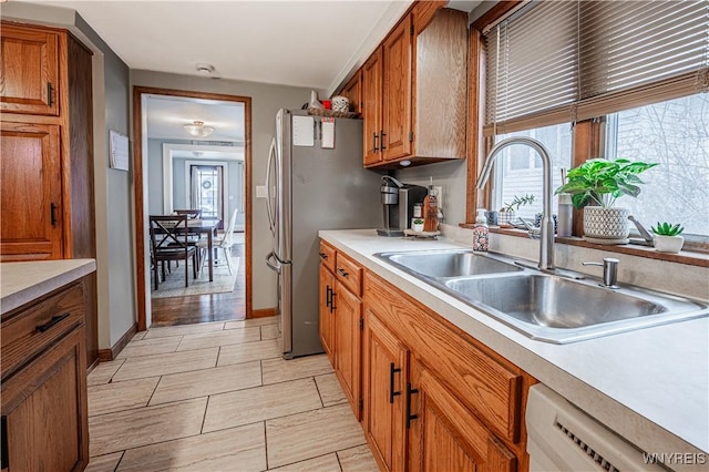 kitchen featuring brown cabinets, freestanding refrigerator, white dishwasher, light countertops, and a sink