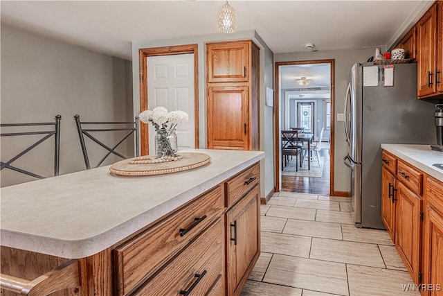 kitchen with a center island, pendant lighting, light countertops, brown cabinetry, and freestanding refrigerator