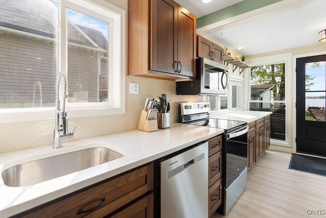 kitchen with light wood-style flooring, stainless steel appliances, a sink, light countertops, and brown cabinets