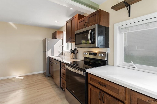 kitchen featuring baseboards, appliances with stainless steel finishes, light countertops, light wood-style floors, and a sink