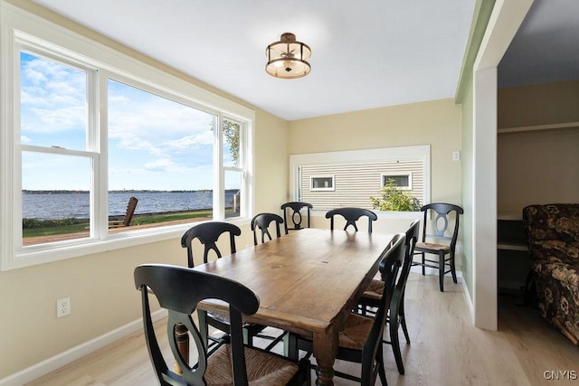 dining area with light wood finished floors, a water view, and baseboards