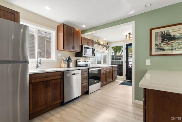 kitchen with recessed lighting, light countertops, appliances with stainless steel finishes, a sink, and light wood-type flooring