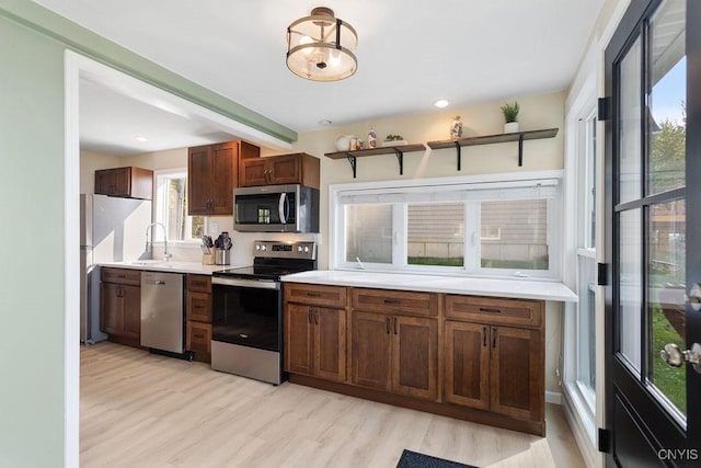 kitchen with beam ceiling, light countertops, appliances with stainless steel finishes, a sink, and light wood-type flooring