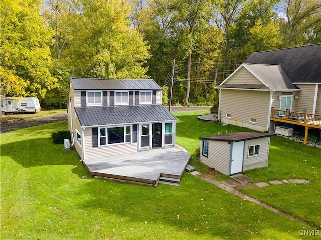 rear view of property with a wooden deck, metal roof, a lawn, and an outdoor structure