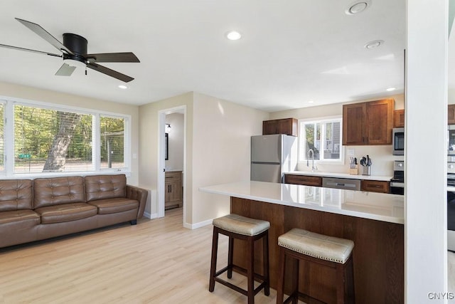 kitchen with light countertops, appliances with stainless steel finishes, light wood-style floors, open floor plan, and a kitchen breakfast bar